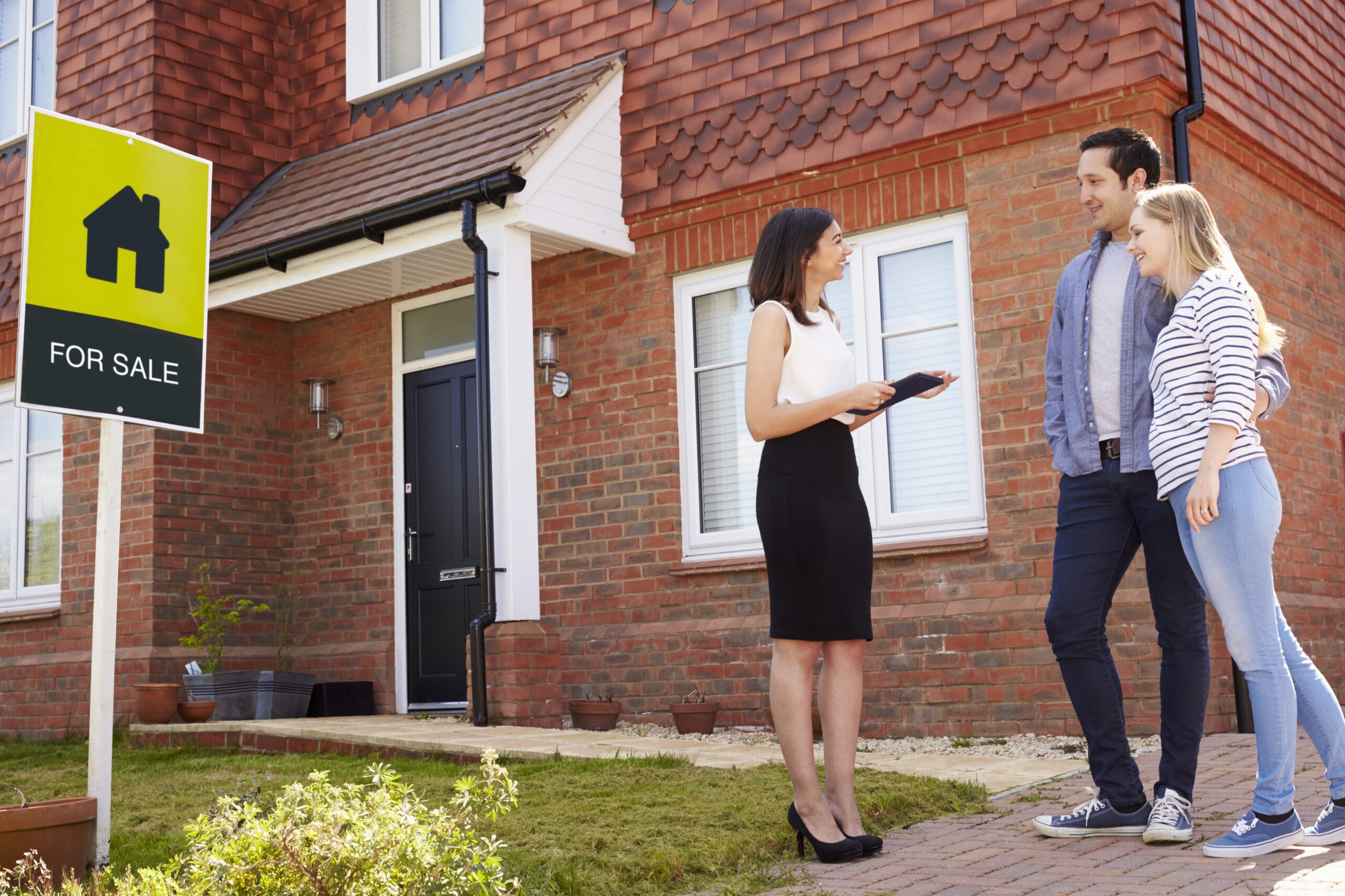 Realtor Outside House For Sale With Young Coupl